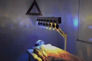 Healing room with color therapy lights for distance energy healing sessions, person lying on treatment table with eye mask, emphasizing relaxation and holistic health benefits, spiritual energy balance, and remote healing techniques.