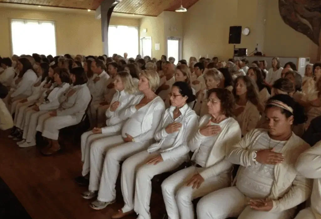 Meditation class, group practicing energy healing, people sitting with hands on their hearts in a serene indoor setting, spiritual wellness and healing workshop, healthy lifestyle, mindfulness activity, promoting mental and emotional balance, tranquility, holistic health, community meditation session, peaceful atmosphere, focused energy healing practice, self-care.