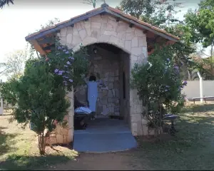 Meditation shrine for distance energy healing outdoor structure with stone walls and roof, surrounded by greenery and flowering bushes, dedicated to spiritual and energy healing practices, peaceful healing space.