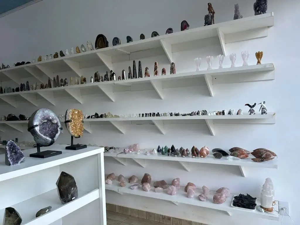 Colorful collection of healing crystals, gemstones, and energy healing tools displayed on white shelves in a wellness center.